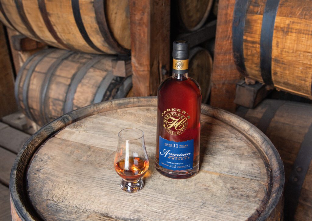 Bottle sitting on a barrel with a Bourbon glass