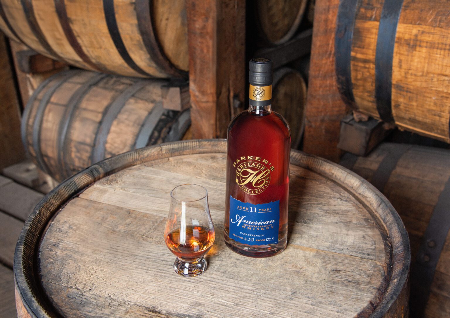 Bottle sitting on a barrel with a Bourbon glass