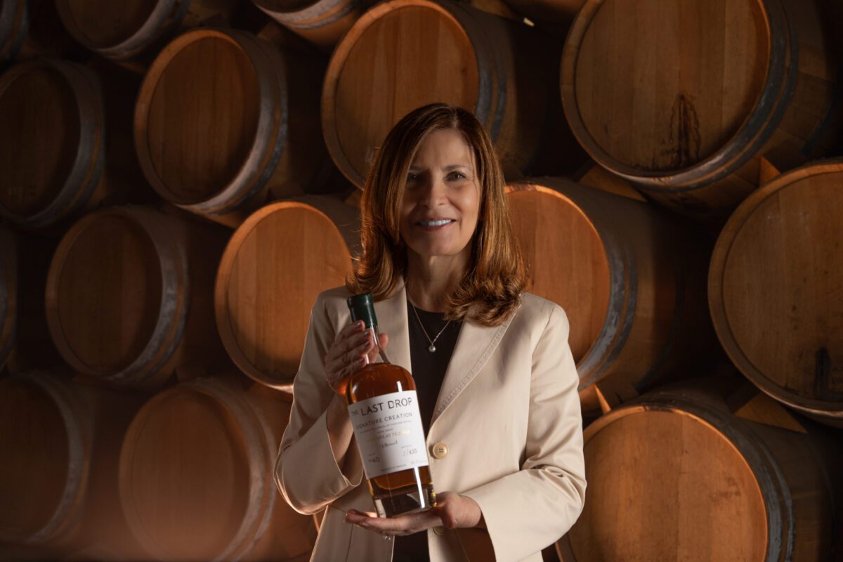 Lady holding a bottle of tequila in front of barrels.